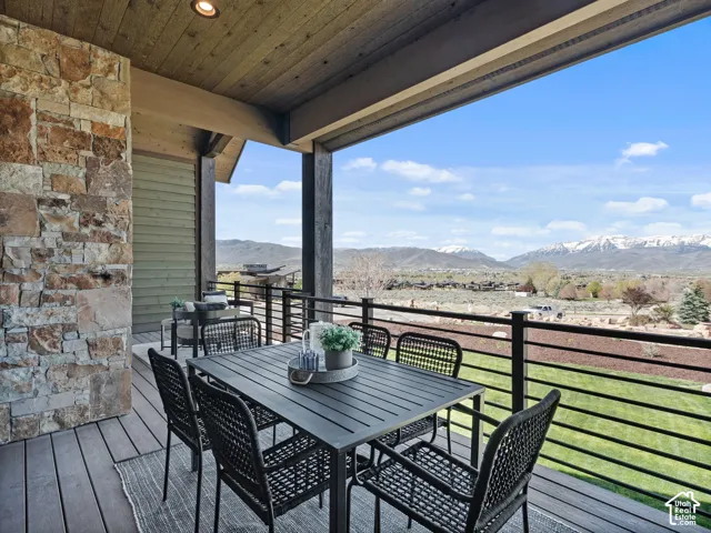 Covered deck featuring wood-plank ceilings, natural stone siding, horizontal metal railings, and mountain scenery