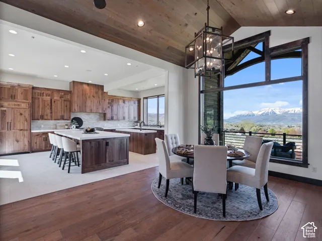 Vaulted wood-plank ceiling, floor-to-ceiling panoramic window with mountain backdrop, custom wood cabinetry, oversized kitchen island with light-toned countertop, and iron lantern-style chandelier