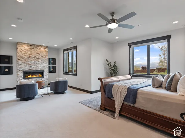 Stone-accented horizontal fireplace, neutral wall-to-wall carpeting, recessed ceiling lighting, ceiling fan with integrated light fixture, and large windows with dark trim
