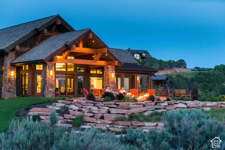 Custom residence exterior featuring exposed timber framing, stone masonry siding, a multi-gabled roofline, and a tiered natural stone retaining wall with an integrated fire feature