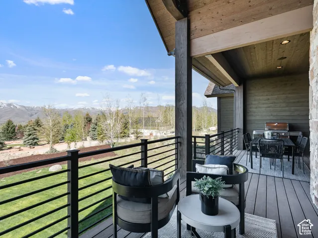 Covered outdoor deck featuring composite decking, dark wood-paneled ceiling, black metal railings, and natural stone exterior wall accents