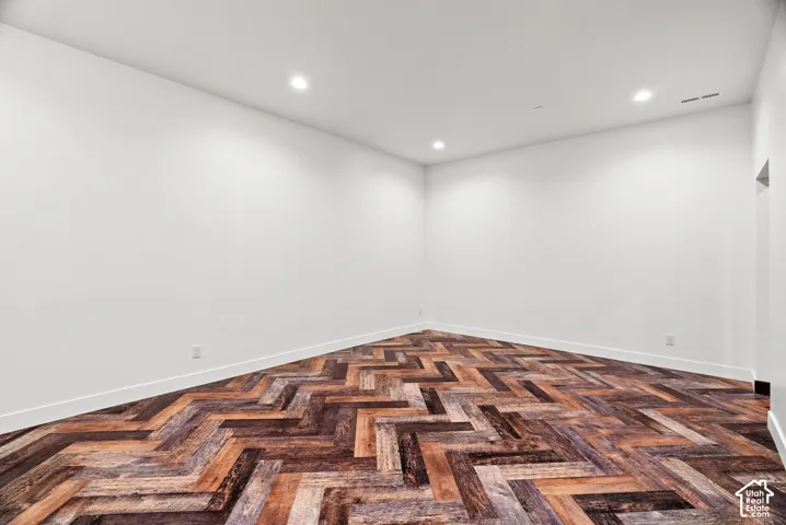 Interior room featuring white walls, recessed ceiling lighting, and wood-finish flooring in a herringbone pattern