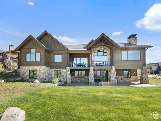Multi-level exterior featuring a combination of horizontal siding and stone masonry, integrated elevated balcony with metal railing, built-in stone fire pit, and multi-gabled roofline