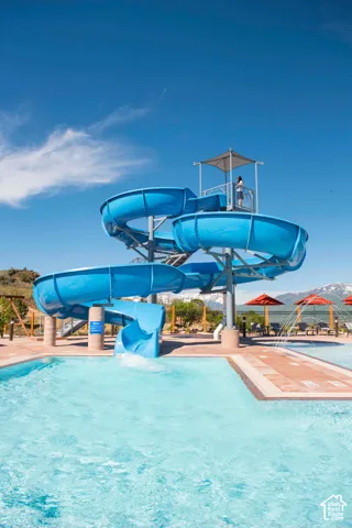 Outdoor swimming pool featuring a spiral water slide, paved pool deck, and mountain backdrop