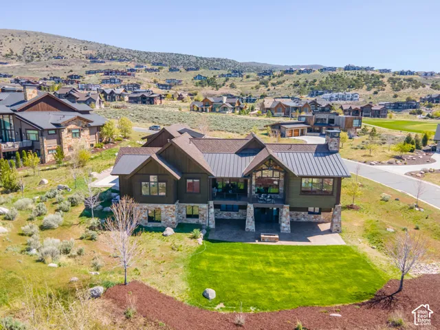 Custom two-story residence featuring wood-plank siding, stone-veneer foundation, metal roofing, expansive rear patio with stone-clad pillars, and integrated fireplace