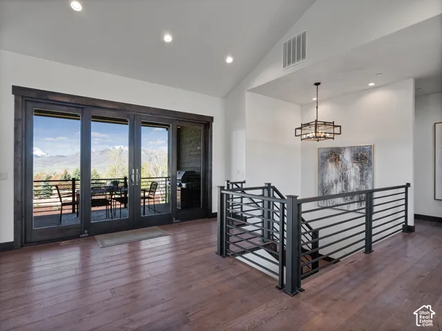 Vaulted ceilings, wood-finish flooring, multi-panel glass doors with dark wood frames, and black metal stair railing featuring horizontal spindles