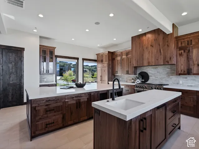 Kitchen featuring dual islands with quartz countertops, custom wood cabinetry, a professional-style range with a matching wood-paneled hood, and light-toned flooring