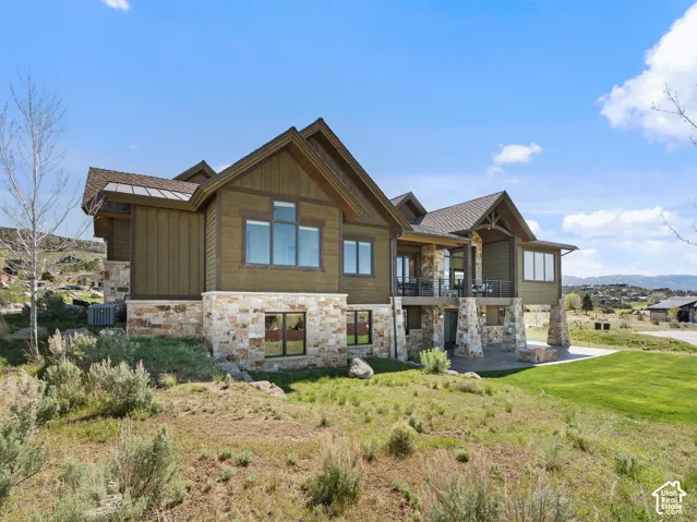 Exterior featuring multi-gabled roofline, stone masonry, wood-finish siding, covered deck, and covered patio