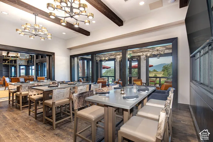 Wood-finish flooring, exposed structural ceiling beams, dual modern multi-light chandeliers, and expansive windows with mountain scenery