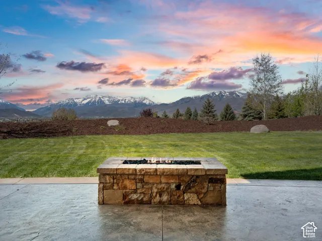 Outdoor space featuring a stamped concrete patio, rectangular stone-veneer fire pit, manicured lawn, and mountainous horizon