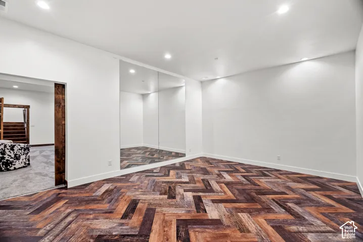 Herringbone-patterned wood-finish flooring, recessed ceiling lighting, and a floor-to-ceiling wall-mounted mirror