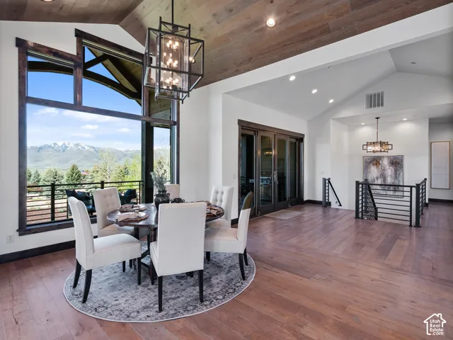 Vaulted ceiling with wood-plank detailing, floor-to-ceiling windows featuring mountain scenery, wood-finish flooring, industrial-style metal lantern lighting, and a metal-railing staircase