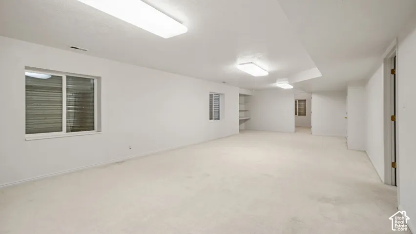 Expansive interior space featuring neutral wall-to-wall carpeting, multiple windows, built-in shelving, and recessed lighting fixtures