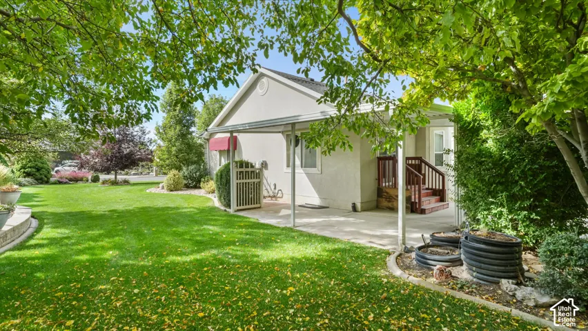Expansive backyard featuring a manicured lawn, mature trees, a concrete patio with a metal awning, and wood-railing stairs