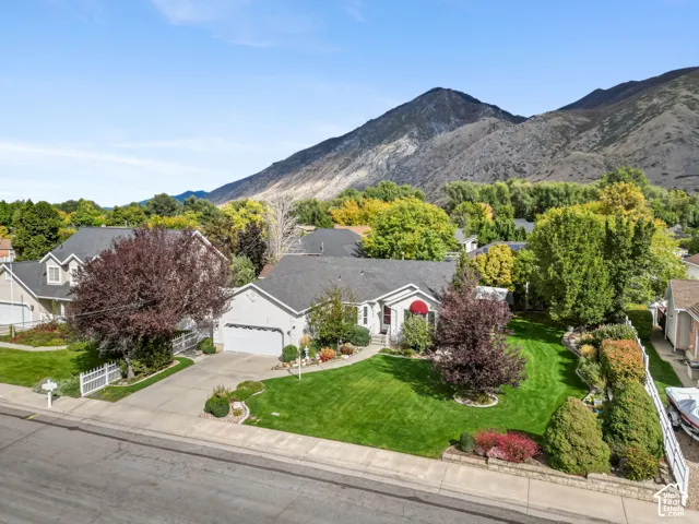 Single-story residence featuring a concrete driveway, two-car garage, manicured lawn, established landscaping, and mountain backdrop