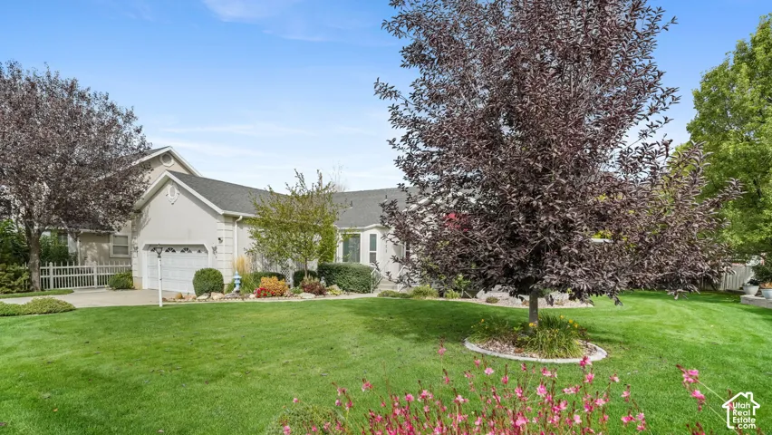 Exterior featuring stucco siding, multi-gabled roofline, two-car garage, manicured lawn, and mature trees