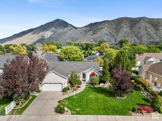 Single-story residence featuring an attached two-car garage, manicured lawn, stone landscaping accents, and a mountain backdrop