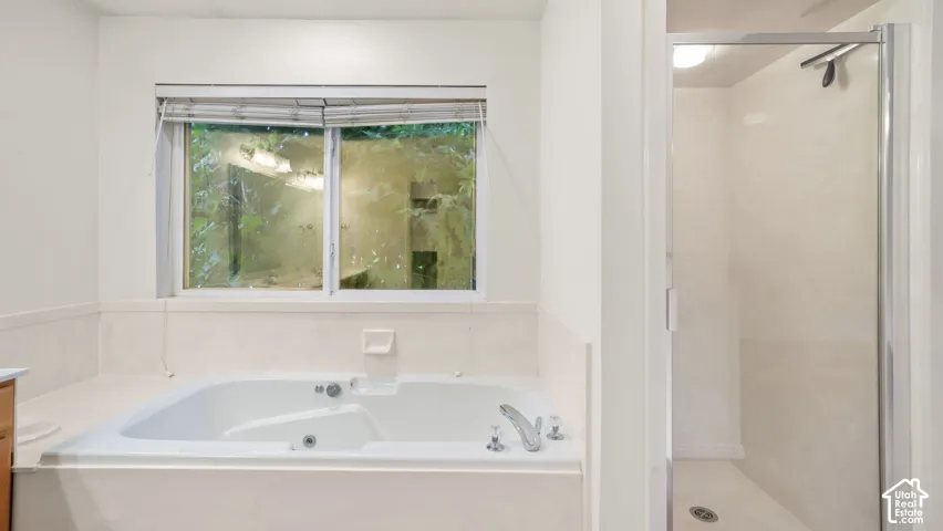 Jetted soaking tub with deck-mounted faucet, separate enclosed glass shower, and tile surround