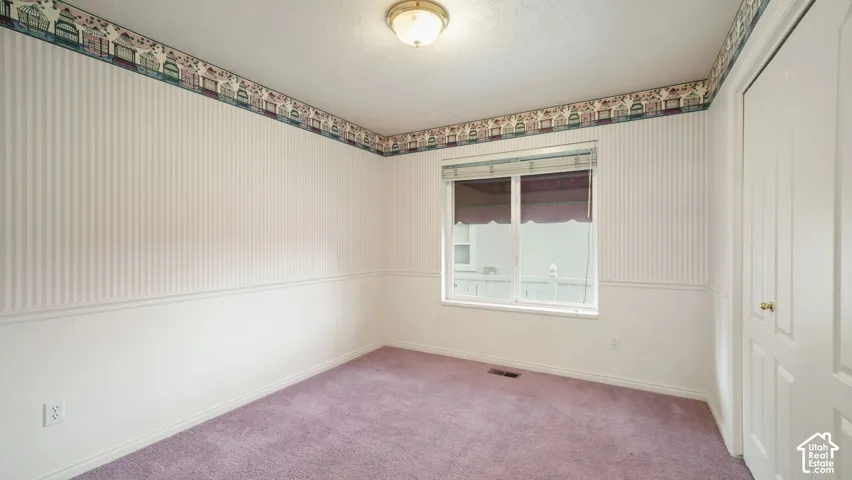 Interior room featuring striped wall coverings, chair rail molding, a double-door closet, carpeted flooring, and a window with a mounted blind