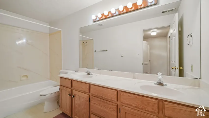 Full-width wall mirror, dual-sink vanity with stone-composite countertop, oak-finish cabinetry, and tub-shower combination with surround