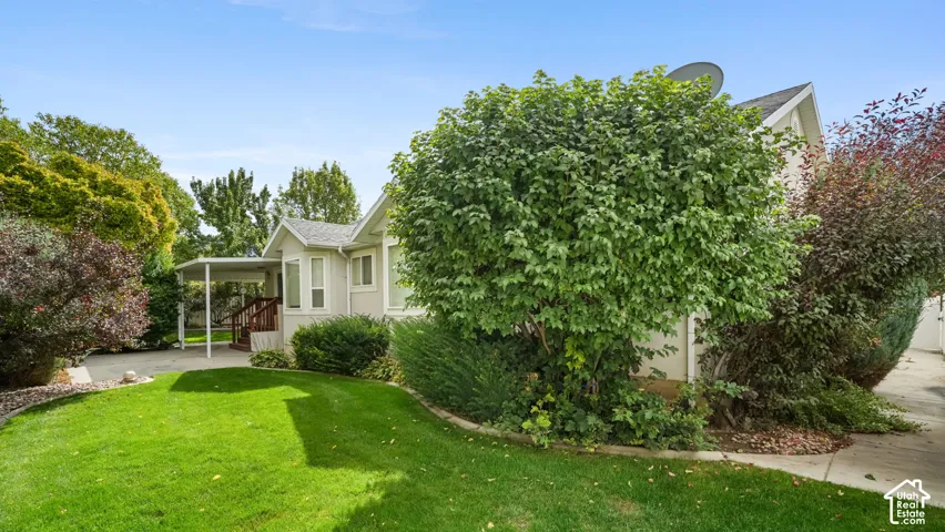 Exterior featuring light-toned siding, a concrete pathway, a covered porch, and landscaped grounds with mature shrubbery