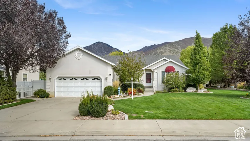 Single-story residence featuring light-toned exterior siding, an attached two-car garage, concrete driveway, and expansive mountain backdrop