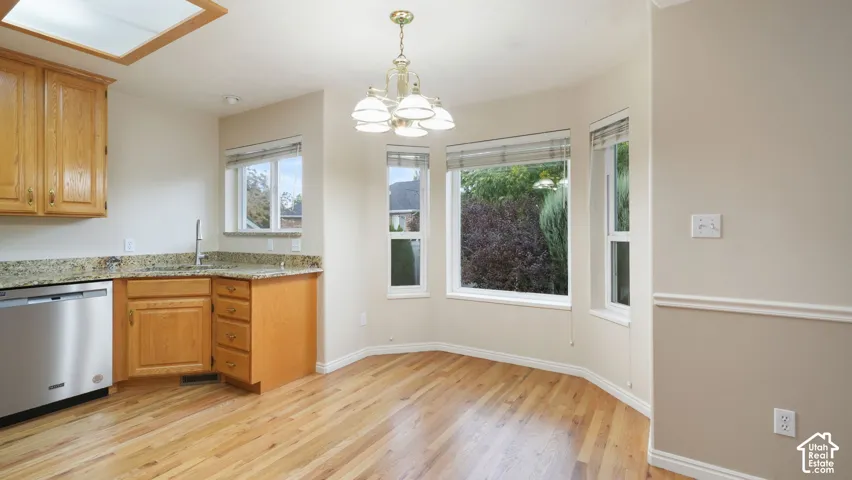 Kitchen area featuring natural wood cabinetry, stone countertops, stainless steel dishwasher, bay windows, and wood-finish flooring