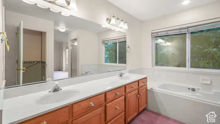 Dual-sink vanity with light-tone wood cabinetry, solid surface countertop, full-width wall mirror, and integrated soaking tub