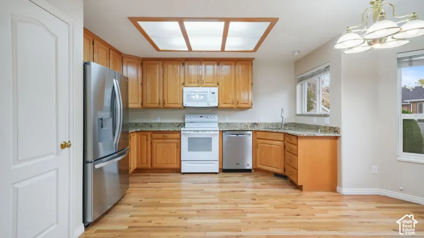 Kitchen featuring wood-finish cabinetry, natural stone countertops, stainless steel appliances, wood-finish flooring, and a recessed ceiling light fixture