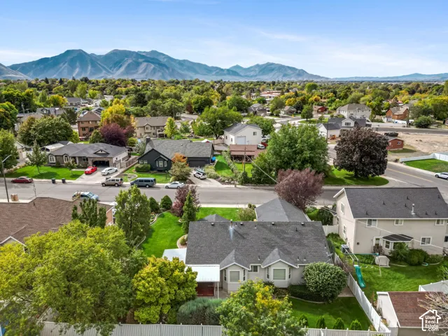 Aerial perspective featuring a multi-gable asphalt shingle roof, manicured lawns, fenced perimeters, and a prominent mountain backdrop