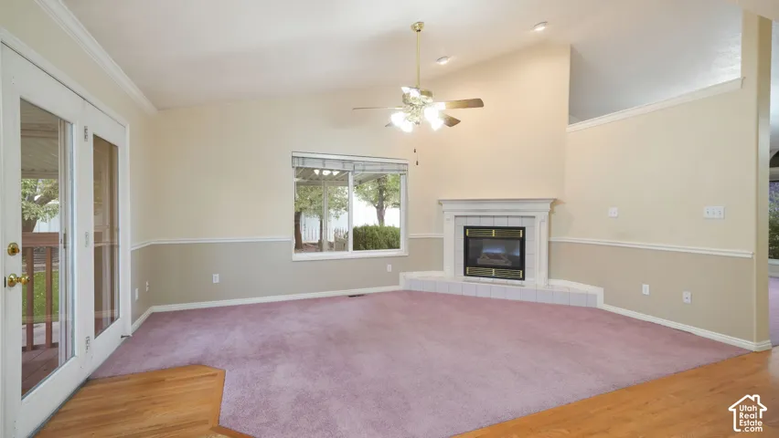 Vaulted ceilings featuring a corner fireplace with a white mantel and tile hearth, complemented by wood-finish flooring, chair rail molding, and French doors