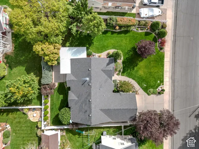 Aerial view of property featuring a sprawling lawn, established landscaping, mature trees, concrete driveway, and white perimeter fencing