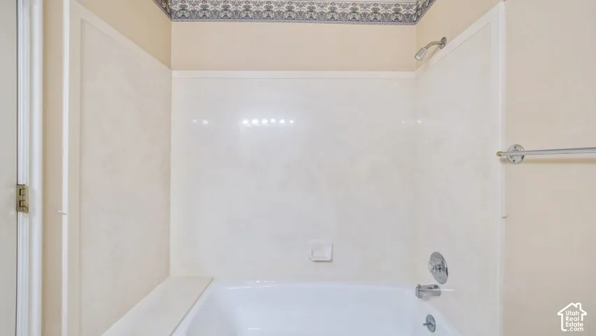 Bathtub featuring a white acrylic surround, chrome shower head, integrated chrome faucet fixtures, and a polished metal towel bar