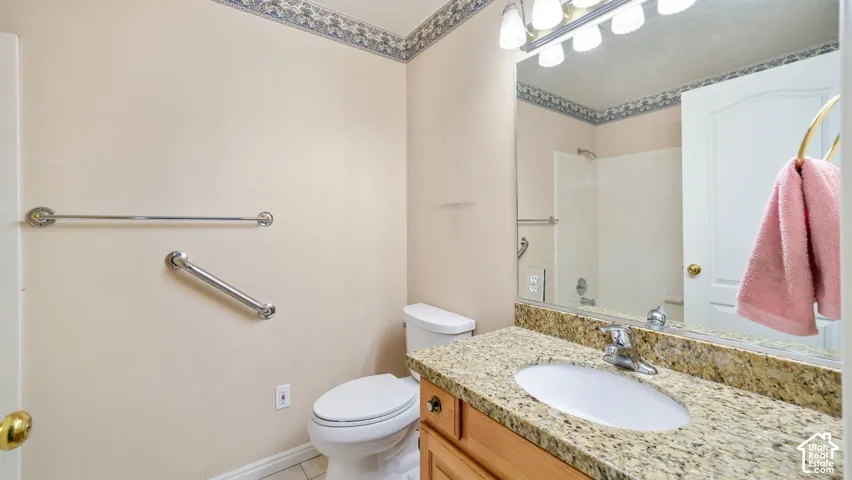 Bathroom featuring a stone-composite countertop, light wood cabinetry, a wall-to-wall mirror, and wall-mounted metal grab bars
