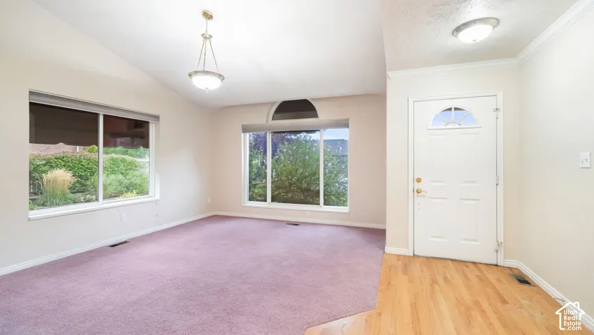 Vaulted ceilings, expansive windows with arched detail, entry door with half-moon glass inlay, wood-finish flooring at entry, and pendant lighting