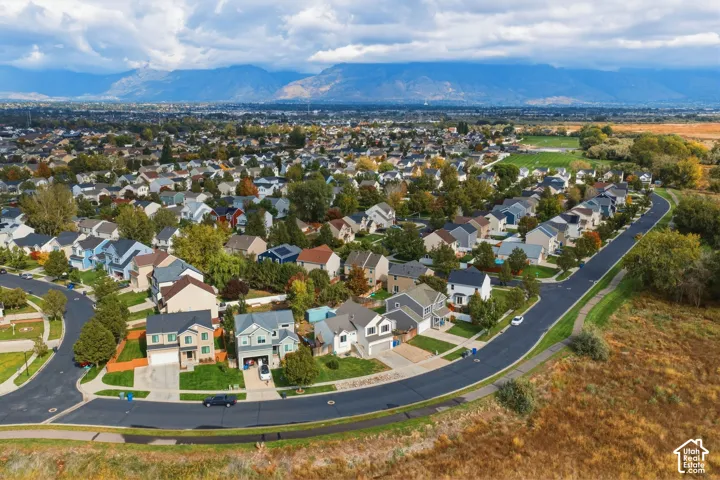 Aerial perspective of a suburban neighborhood featuring paved streets, established green landscaping, and a prominent mountain range backdrop