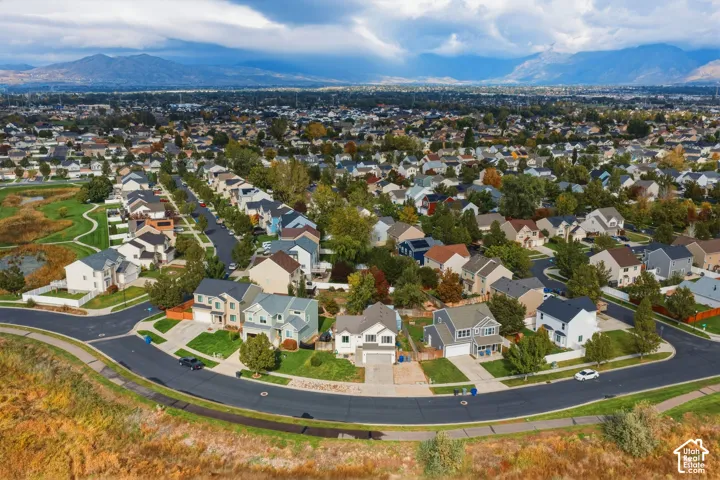 Aerial perspective featuring suburban residential housing, paved streets, manicured green spaces, and a mountain range backdrop