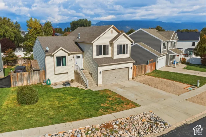Two-story residence featuring light-colored siding, a multi-gable roofline, an attached two-car garage, concrete driveway, and a front lawn with mountain backdrop