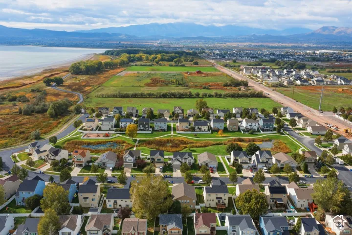 Aerial perspective featuring a landscape of open green space, mature trees, a central pond, and distant mountain backdrops