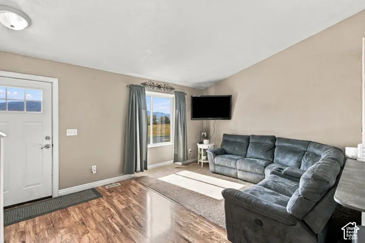 Living area featuring vaulted ceilings, wood-finish flooring, a neutral color palette, and a large window with mountain scenery
