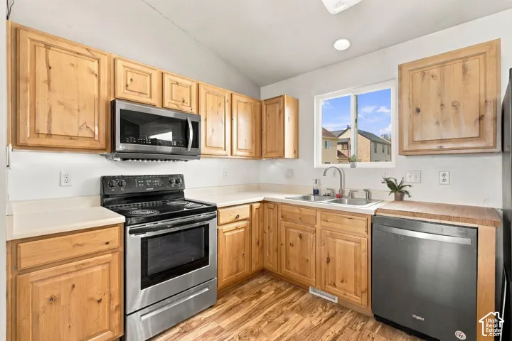 Kitchen featuring natural wood cabinetry, stainless steel appliances, solid surface countertops, a double-basin sink, and wood-finish flooring