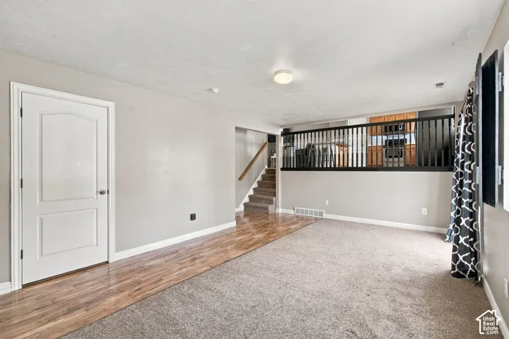 Neutral interior space featuring wood-finish flooring, wall-to-wall carpeting, a multi-panel interior door, and a black metal spindle railing