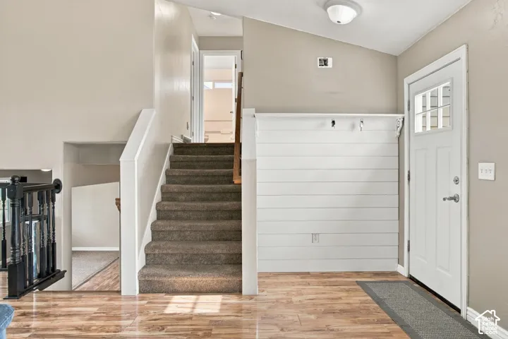 Entryway featuring wood-finish flooring, white shiplap accent wall with built-in hooks, carpeted staircase, and white paneled entry door with glass insert