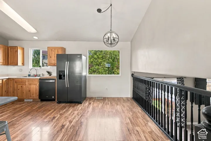Kitchen area featuring wood-finish cabinetry, black appliances, wood-finish flooring, a spherical pendant light fixture, and a black-painted staircase railing