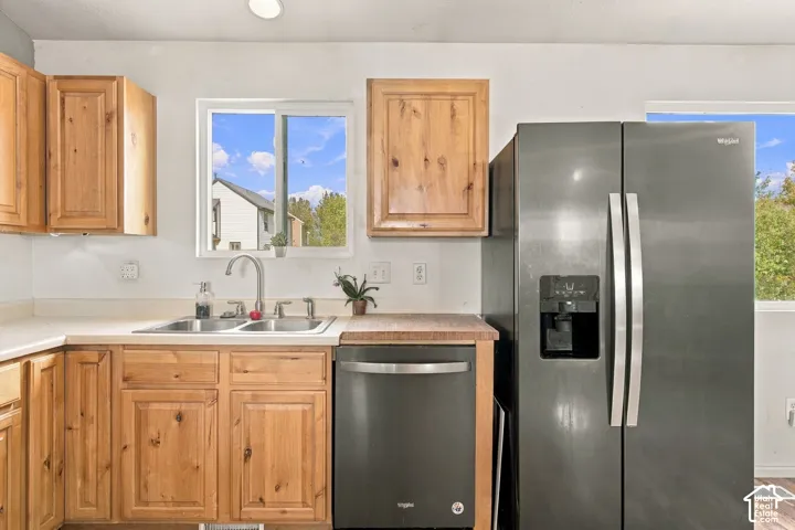 Kitchen featuring natural wood cabinetry, stainless steel sink with pull-down faucet, dark-finish appliances, and a rectangular window