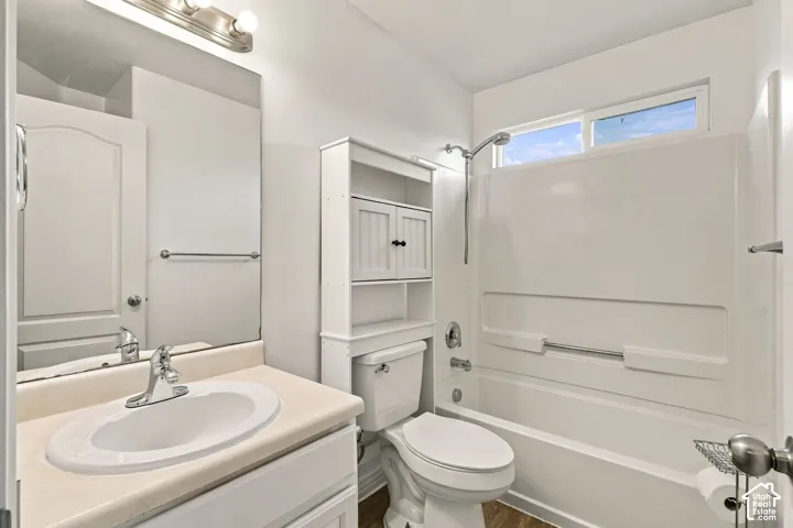 Bathroom featuring a vanity with a drop-in sink, wall-mounted mirror, built-in shelving unit, tub-shower combination with a detachable showerhead, and a rectangular transom window