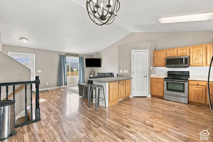 Open-concept space featuring vaulted ceilings, wood-finish flooring, a kitchen island with stone countertop, and a decorative orb chandelier