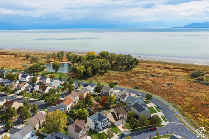 Aerial perspective of a residential community featuring expansive natural landscapes, mature trees, a shoreline water proximity, and mountain backdrops