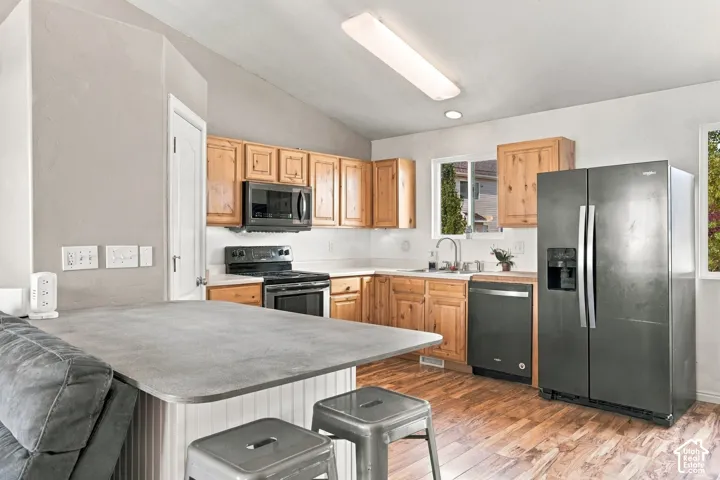 Kitchen featuring wood cabinetry, solid-surface countertops, vaulted ceilings, wood-finish flooring, and black appliances