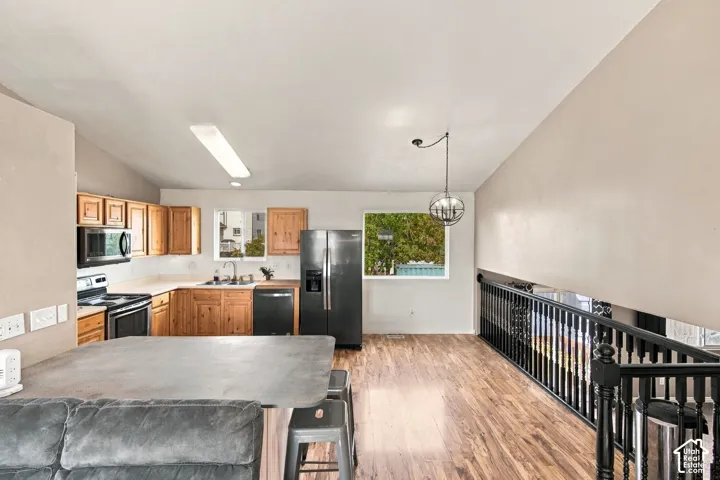 Kitchen featuring wood cabinetry, solid-surface countertops, black appliances, wood-finish flooring, and a vaulted ceiling with an orb pendant light